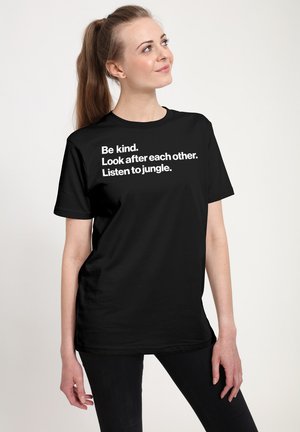Sort t-shirt med korte ærmer med hvid tekst: "Vær venlig. Pas på hinanden. Lyt til junglen." Glat tekstur, afslappet pasform.