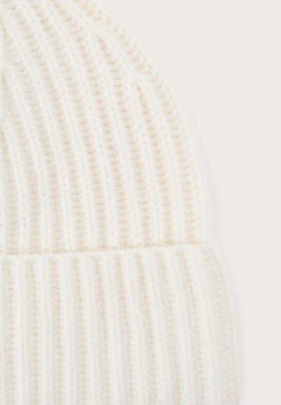 Strikket lue i myk hvit ull, med vertikal ribbet tekstur og en brettet mansjett nederst. Glatt finish og lett design.