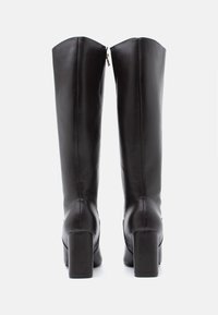 Μαύρες δερμάτινες μπότες μέχρι το γόνατο με τετράγωνη φτέρνα και κάθετη λεπτομέρεια φερμουάρ στο πίσω μέρος. Λείος υφασμάτινος τύπος, δομημένο σχήμα.