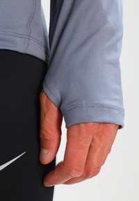 Ljusblå långärmad skjorta med en åtsittande manschett, visas tillsammans med svarta träningsbyxor med en vit logotyp och en slank design.