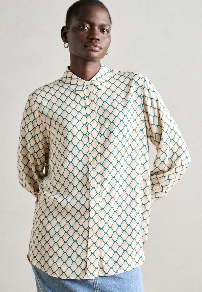 Button-up shirt in cream with a geometric teal pattern, featuring a classic collar, long sleeves, and a relaxed fit. Soft fabric texture.