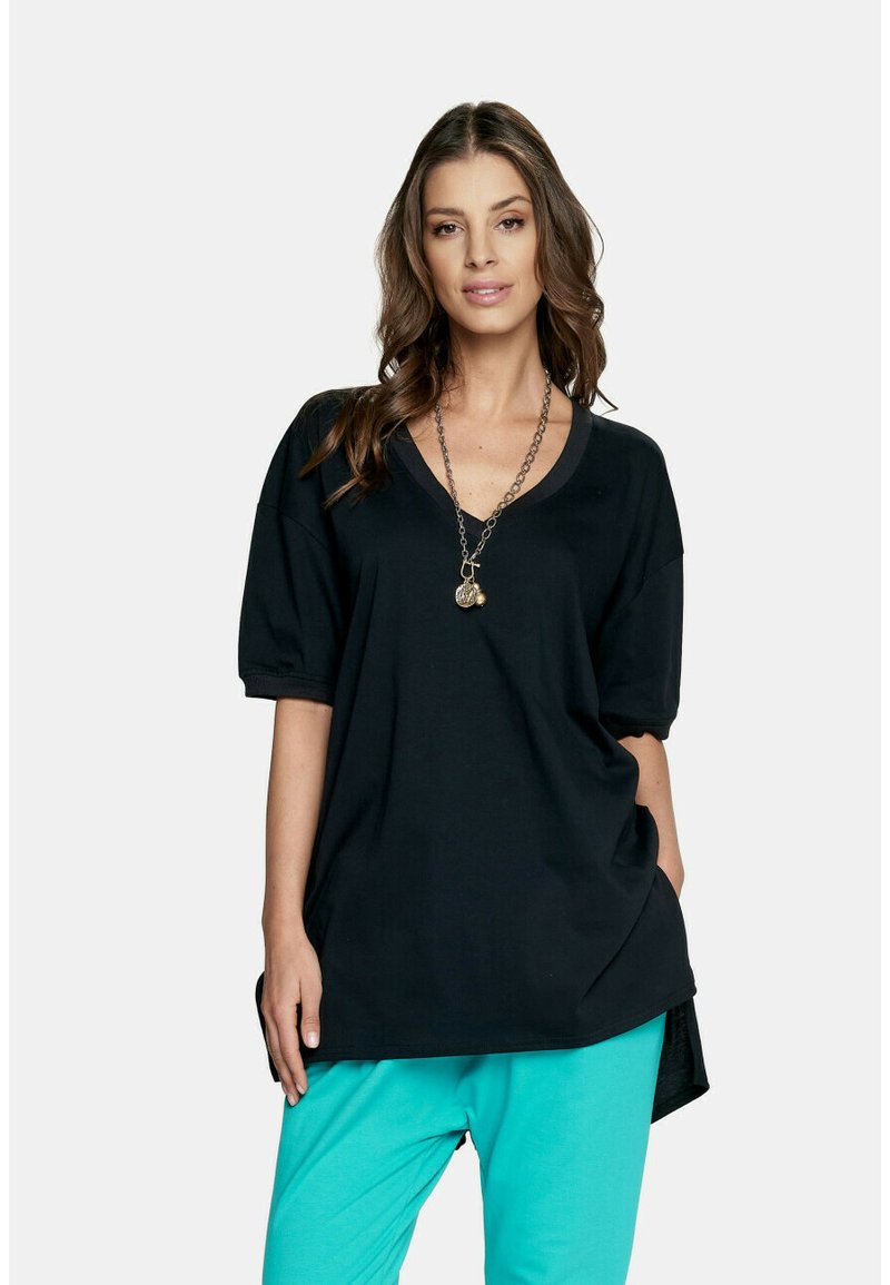 Czarny, oversize t-shirt z bawełny z głębokim dekoltem w kształcie litery V i krótkimi, bufkowymi rękawami. Noszony z turkusowymi spodniami i uzupełniony łańcuszkiem jako biżuterią.
