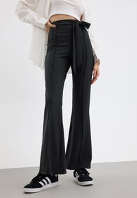 Pantalons évasés à rayures noires et blanches avec une taille à lacer. Comprend un matériau texturé et une surface lisse. Associés à des baskets noires.