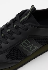 Černé tenisky s černou síťovinou a tkaničkami, olivově zelenou podešví a pruhem, logo EA7 Emporio Armani na bočním panelu.