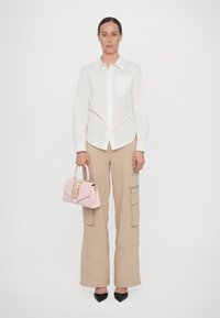 Vit skjorta, beige cargo-byxor med fickor, rosa handväska med guldfästen och svarta spetsiga klackskor. Släta ytor.