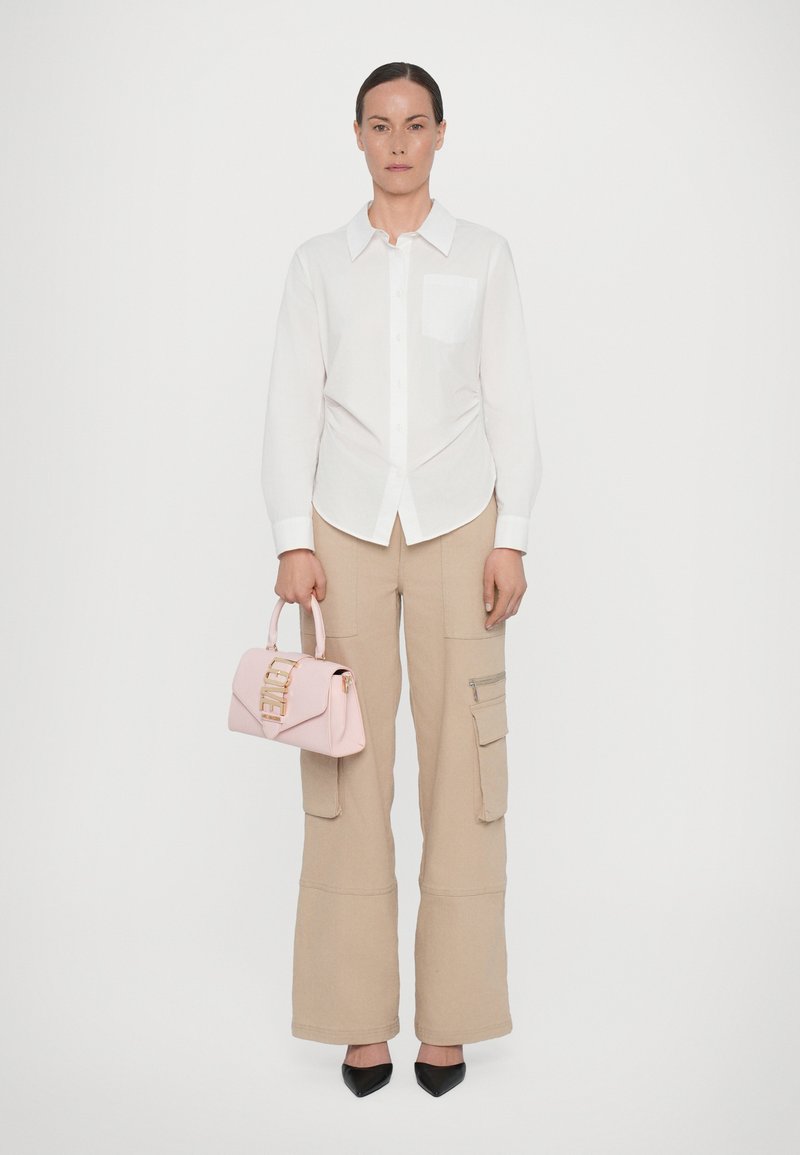 Vit skjorta, beige cargo-byxor med fickor, rosa handväska med guldfästen och svarta spetsiga klackskor. Släta ytor.