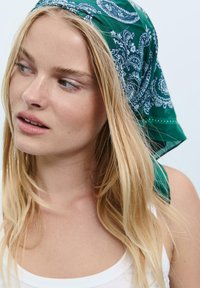 Grøn bandana med hvid paisley mønster, lavet af letvægtsstof, bundet rundt om hovedet og delvist dækkende blonde hår.