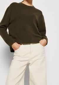 Olivgrön stickad tröja med rund halsringning och ribbade ärmslut, i kombination med krämfärgade byxor med vida ben och sidfickor.