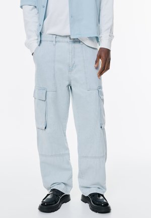Helle blaue Cargo-Shorts aus Denim, mit mehreren Taschen, einem lässigen Schnitt und genähten Details. Kombiniert mit schwarzen Schuhen.
