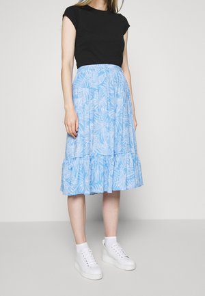 Jupe midi bleu clair à motifs floraux avec un ourlet volanté, assortie d'un haut noir ajusté et de baskets blanches à semelle épaisse.