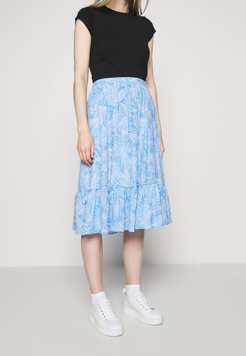 Jupe midi bleu clair à motifs floraux avec un ourlet volanté, assortie d'un haut noir ajusté et de baskets blanches à semelle épaisse.