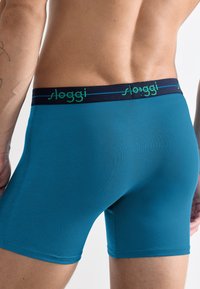 Turkusowe slipy bokserki z granatowym pasem, na którym znajduje się zielone logo "sloggi". Gładka tekstura i przylegający krój zwiększają komfort i wsparcie.