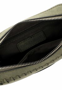 Pochette in suede verde oliva con fodera in tessuto nero, dotata di chiusura con zip e cucitura decorativa lungo il bordo. Contiene una piccola tasca interna.