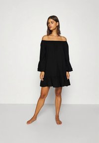 Õlgadest paljastav must kleit, millel on pikad kellukakujulised varrukad, volangidega ääreosa ja voolav disain, valmistatud kerge kangaga.