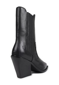 Stivale alla caviglia in pelle nera stile western con tacco a blocco e pannelli laterali elasticizzati cuciti su sfondo bianco.