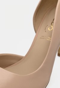 Beige skinn høye hæler med rund tå og en glatt finish. Har en subtil glans og en kort blokkhæl. Gullfarget innvendig merke.