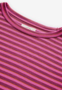 Gros plan sur l'encolure d'une chemise rayée rose et violette avec des coutures visibles et une étiquette blanche partiellement visible.