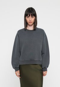 Dark gray sweatshirt with a crew neck, loose fit, ribbed cuffs, and a clean design, paired with an olive green, form-fitting skirt.
