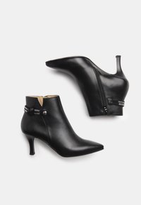 Zwarte leren enkelboots met een spitse neus, stiletto-hak en een zijrits. Beschikt over decoratieve hardware op de enkel en een gladde textuur.
