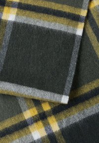 Coperta di lana con un motivo a quadri verde, giallo e grigio. Il tessuto è morbido, con una superficie texture e fibre pelose visibili.