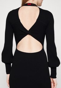 Schwarzes, geripptes Longsleeve-Kleid mit tiefem V-Ausschnitt am Rücken und einem Twist-Detail. Es hat Puffärmel und eine taillierte Taille für eine schlanke Silhouette.