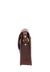 Brūns ādas plecu soma redzama no sāniem ar redzamu zelta toņa aparatūru un izšūtiem detalizējumiem uz balta fona.