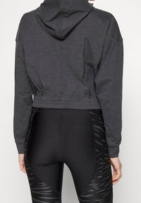 Grå kort hoodie med dragsko på huooden, med avslappnad passform och elastisk nederkant. Tillsammans med svarta leggings med tigerstripemönster.