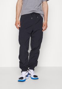 Svarta lätta joggers med ett elastiskt midjeband, smalnande ben och subtil textur. Kombineras med vita och blå sportiga sneakers.