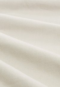 Tissu beige clair avec un tissage texturé, présentant une finition douce et légèrement brillante. La surface est lisse avec de subtiles variations tonales.