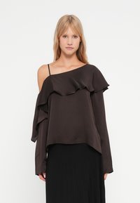 Top asimmetrico marrone scuro con design arricciato, maniche lunghe e una sola cinghia sulla spalla, realizzato in tessuto liscio.