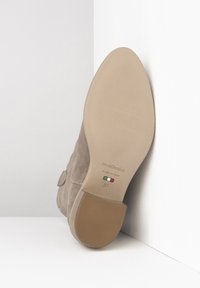 Bottine en daim beige montrant une semelle en caoutchouc plate et texturée avec un léger talon. L'étiquette indique "NeroGiardini", "Fabriqué en Italie" et taille 37.