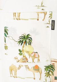 Tela blanca con un estampado colorido de camellos y palmeras. Incluye un bolsillo decorativo y una etiqueta de marca en el lateral.