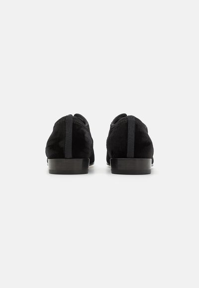 Chaussures en daim noir avec un talon bas, présentant une texture lisse, un bout arrondi et des détails élastiques à l'arrière pour un enfilage facile.