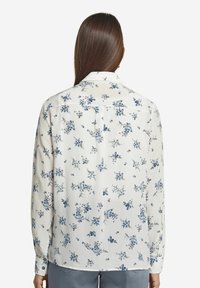 Långärmad skjorta i lätt tyg, vit med blå blommönster, med knapp-halskrage och manschetter, rak fåll och ryggveck.