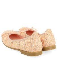 Bailarinas de melocotón brillantes con puntas redondas, pequeños lazos decorativos y suelas de goma marrón claro, mostradas desde ángulos traseros y laterales.