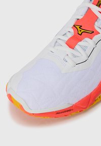 Chaussure de course blanche avec un dessus texturé et des accents rose vif. Présente une semelle jaune et des finitions noires avec une marque clairement visible sur le côté.