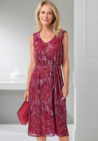 Kleid mit rotem und lila Blumendruck, V-Ausschnitt, ärmellosem Design, plissierter Textur und Taillengurt. Begleitet von einer pinken Clutch.