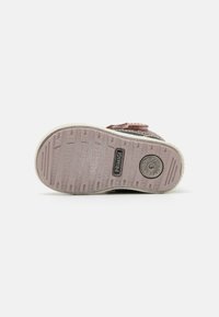 Semelle de chaussure avec une base en caoutchouc rose texturé, présentant des nervures et un logo circulaire. Bords renforcés et marquage en relief sur la surface.