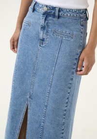 Denim maxi skirt in light blue with front slit, detailed stitching, two front pockets, and a classic button closure at the waist.