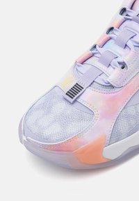 Gros plan sur la zone des orteils d'une chaussure de sport avec des accents rose pastel, violet et orange et des lacets épais sur une tige en mesh gris.