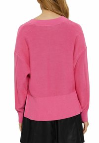 Różowy sweter dzianinowy o luźnym kroju, z prążkowanym wykończeniem u dołu i na mankietach oraz opadającymi ramionami dla zwiększenia komfortu.