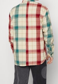 Langærmet flannel skjorte med et ternet mønster i rød, teal og creme. Fremstillet af blødt stof med knaplukning ved håndleddene og krave.