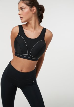 Zwarte sportbh met een gestructureerd ontwerp, voorzien van een bovenpaneel van mesh, witte accentstiksels en brede schouderbanden. Gecombineerd met high-waisted leggings.