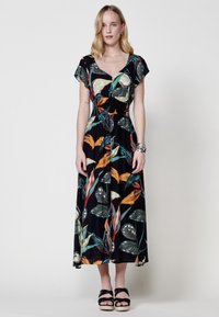 Vestido maxi con fondo negro que presenta coloridos patrones de hojas tropicales. Mangas cortas ajustables y un cuerpo ceñido con una falda acampanada.