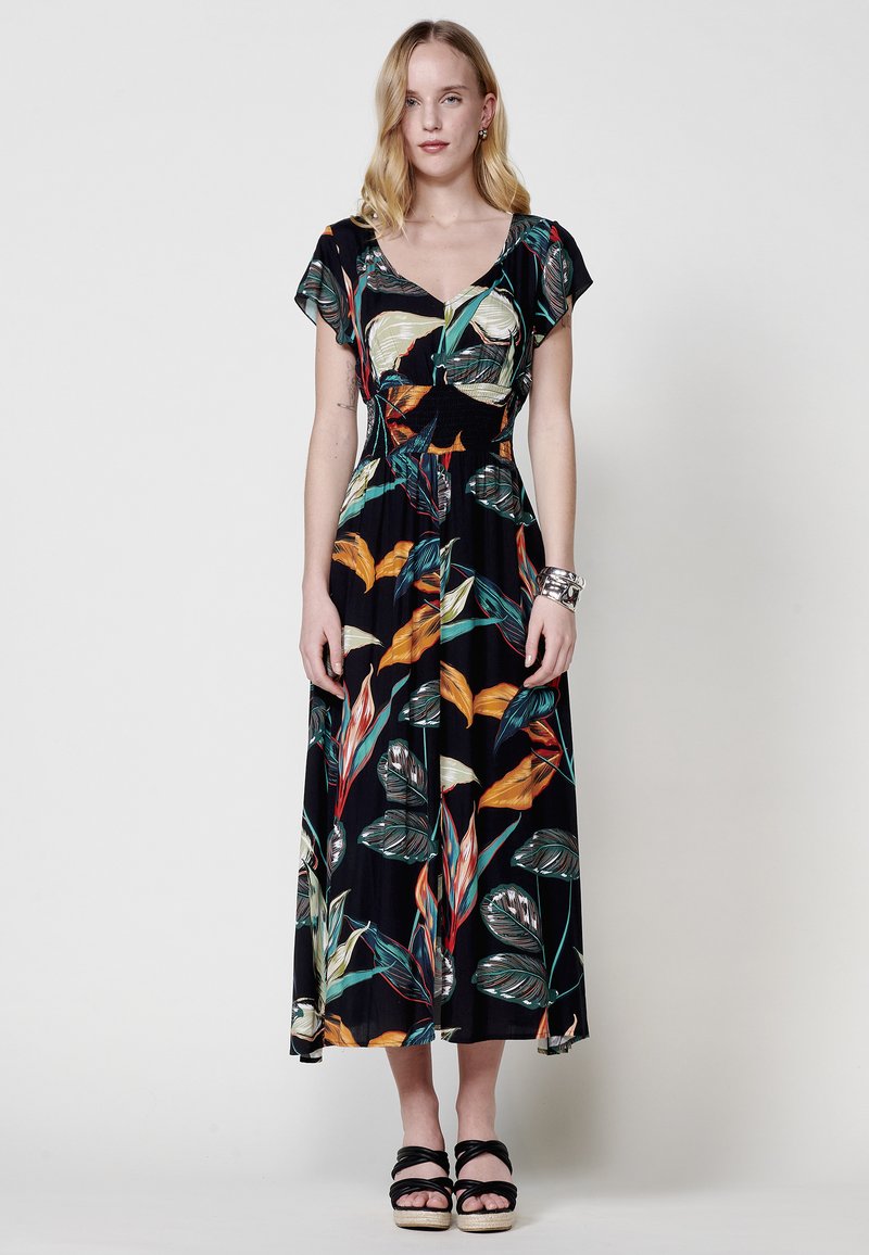 Vestido maxi con fondo negro que presenta coloridos patrones de hojas tropicales. Mangas cortas ajustables y un cuerpo ceñido con una falda acampanada.