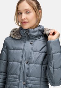 Ocieplana szara kurtka z kapturem z sztucznego futra, z wysokim kołnierzem, zapięciem na zamek błyskawiczny i czarnymi guzikami jako akcentami. Gładka tekstura i pikowany wzór.