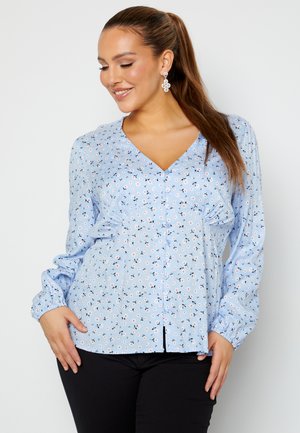 Blusa floreale azzurro chiaro con chiusura a bottoni, maniche lunghe e texture arricciata. Presenta piccoli fiori sparsi in rosa e blu navy.