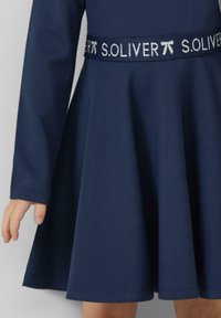 Granatowa sukienka z długimi rękawami i rozkloszowanym dołem. Zawiera błyszczącą taśmę z logo wokół talii oraz gładką strukturę materiału.