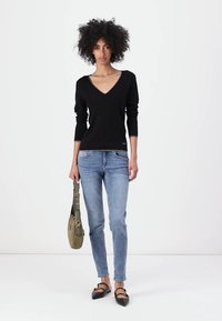 Maglione nero a V con maniche lunghe, jeans aderenti azzurri, ballerine nere e borsa a spalla verde. Design semplice e moderno.