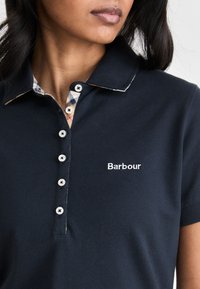 Ναυτική κοντομάνικη πόλο μπλούζα με σχέδιο γιακά, που διαθέτει καρό μοτίβο κάτω από τον γιακά και λευκό κεντητό λογότυπο.